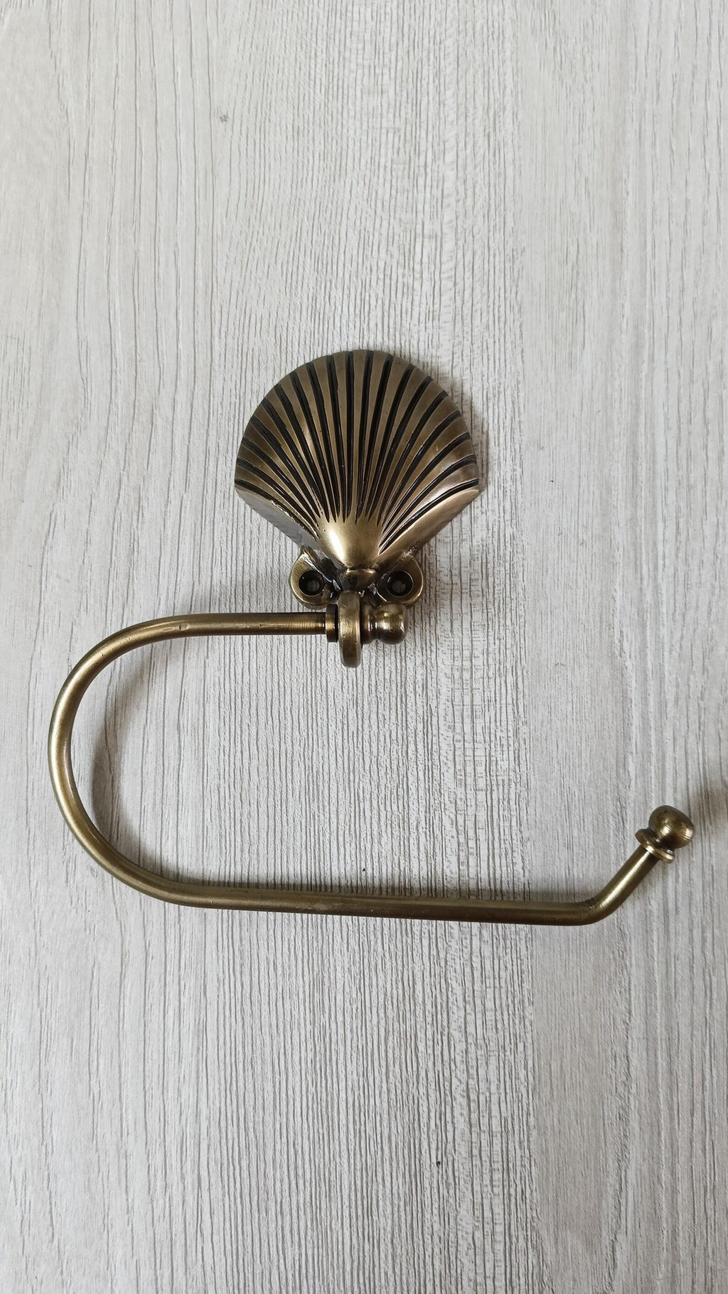 Brass seashell toilet paper holder with curved arm and ball end cap, shown without a roll