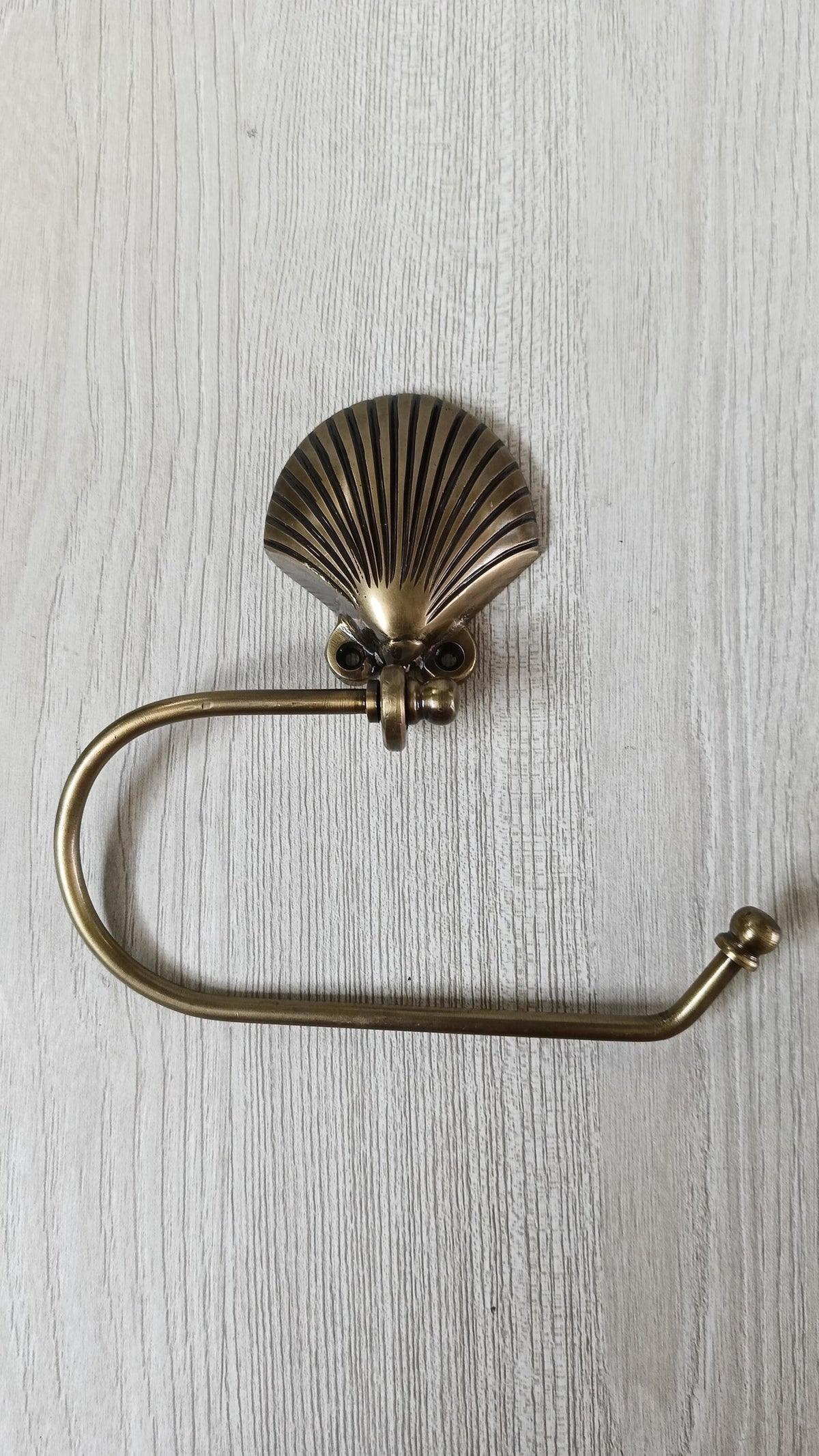 Brass seashell toilet paper holder with curved arm and ball end cap, shown without a roll