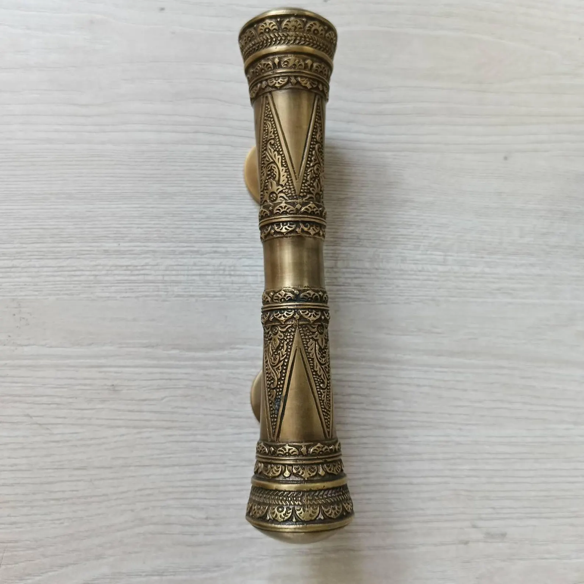 Front view of the engraved brass pull handle lying flat on light wood