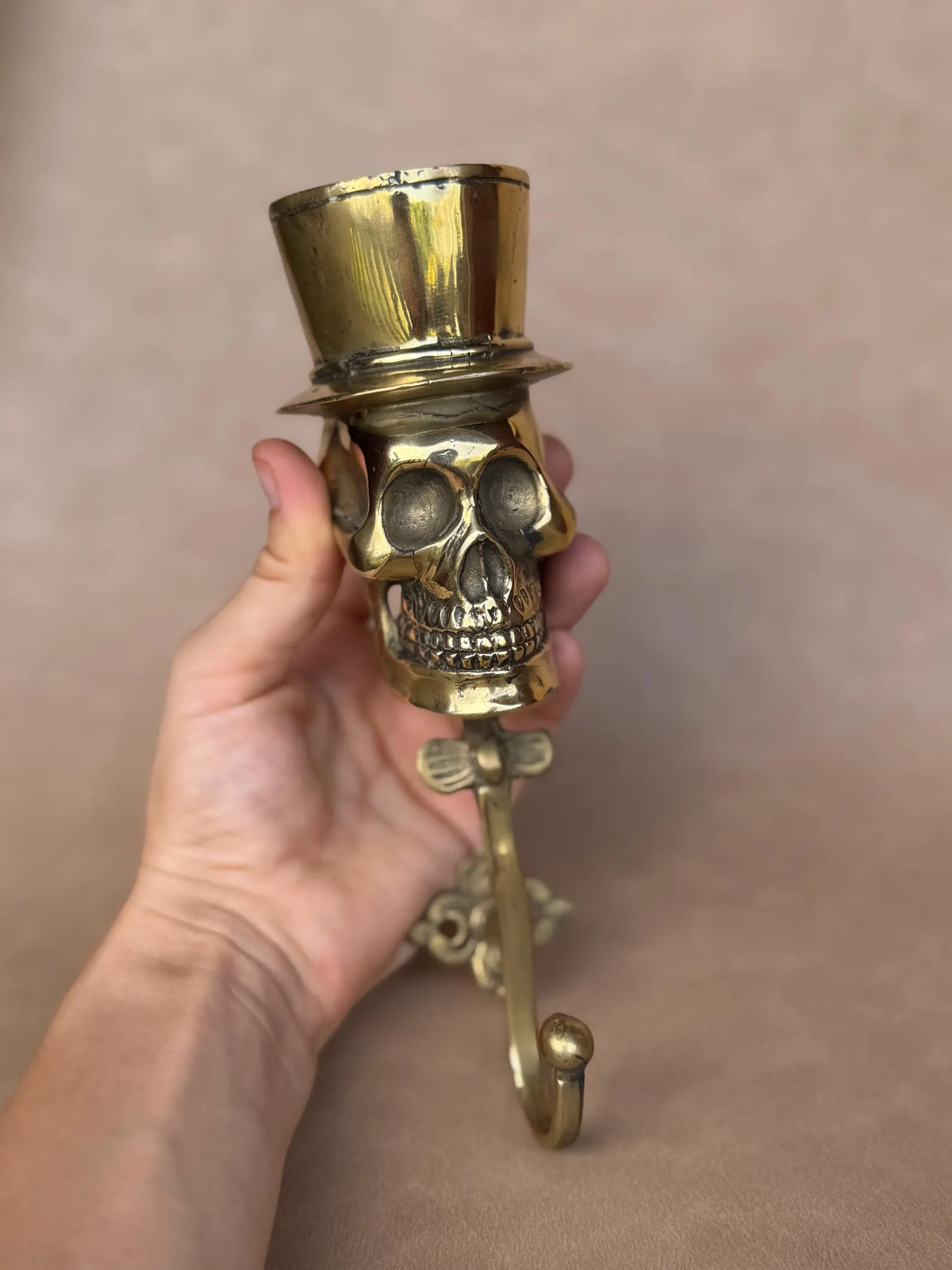 Brass skull hook with top hat and decorative backplate, slightly angled front view