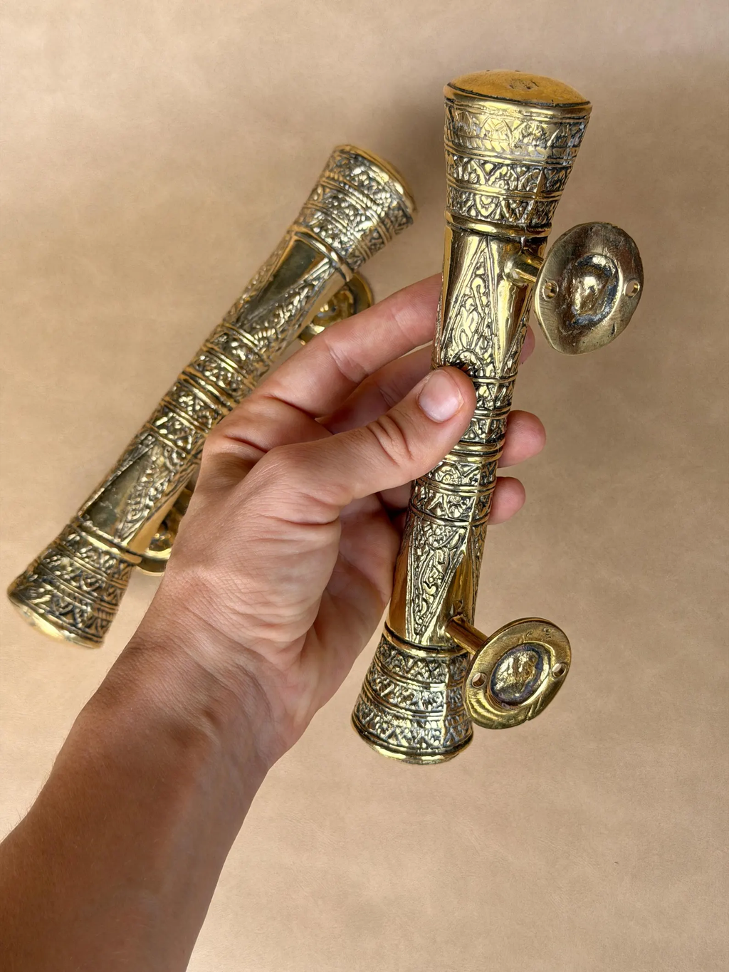 Hand holding two engraved brass pull handles of different lengths