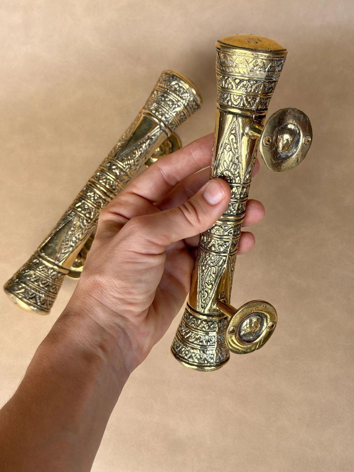 Hand holding two engraved brass pull handles of different lengths