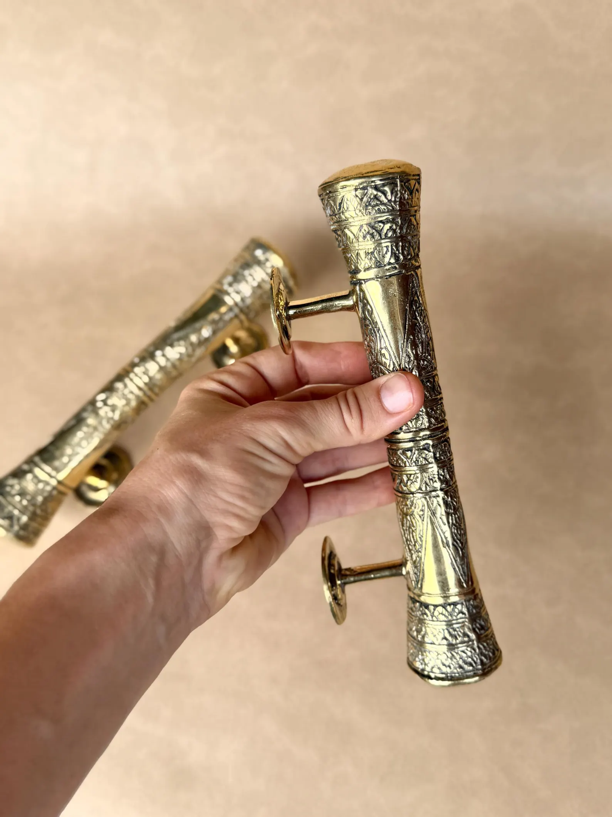 Hand holding an engraved brass pull handle next to a smaller one