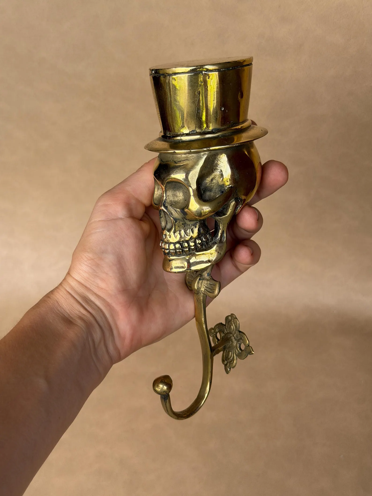 Brass skull top hat hook at a three-quarter angle, showing the ornate mounting plate