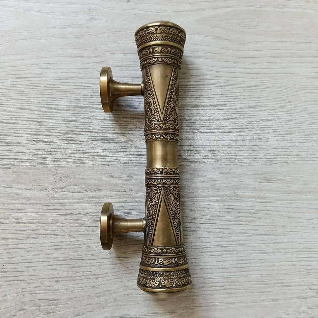 Brass oriental door pull handle with two mounting posts, side view on light wood
