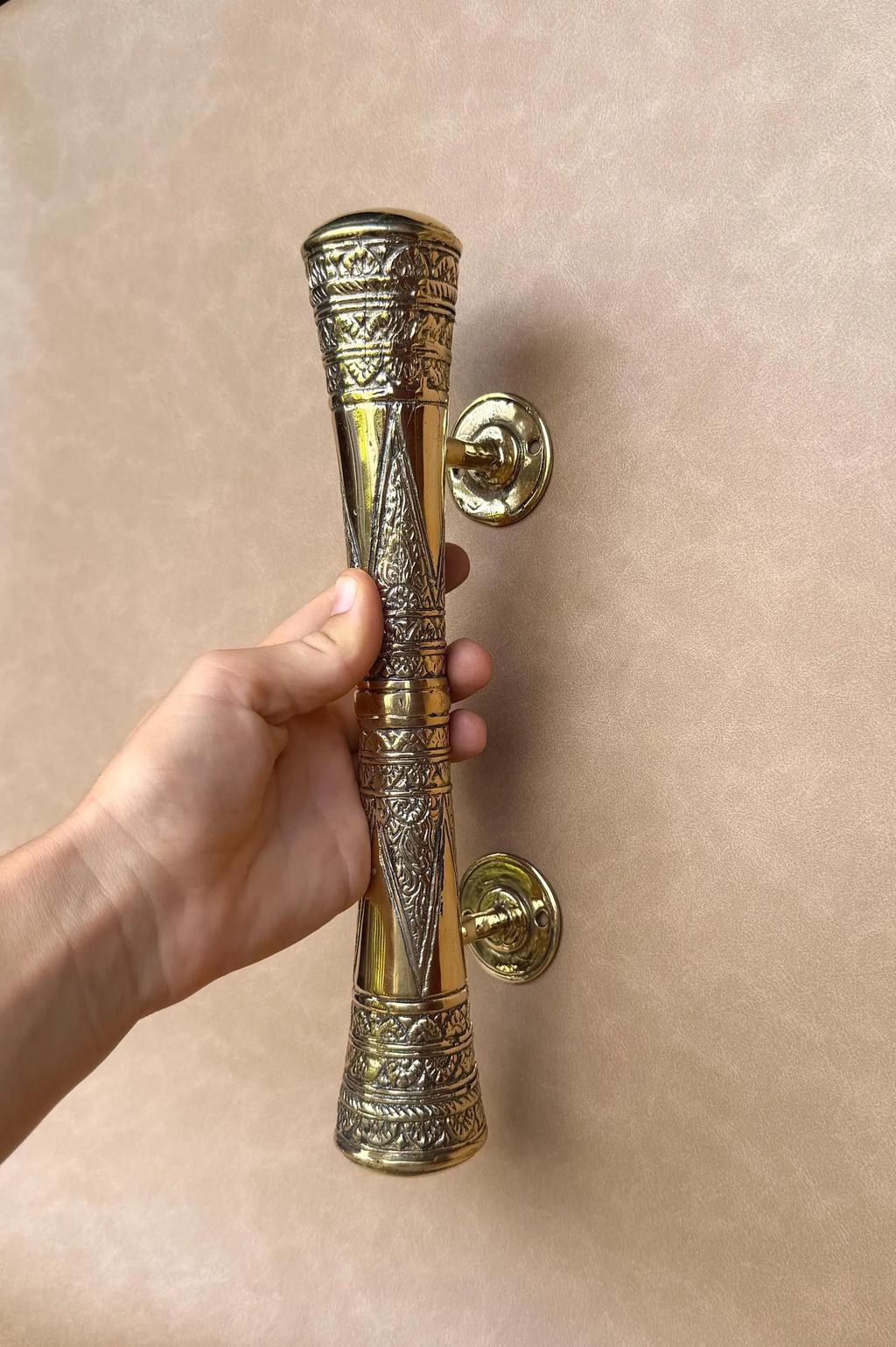 Hand holding the long brass oriental door pull upright