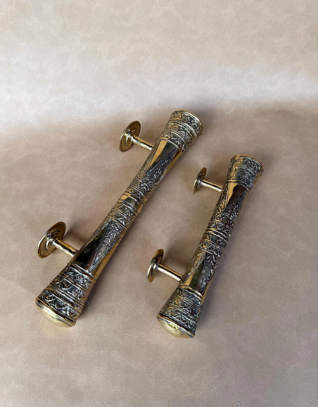 Two brass pull handles lying with mounting posts facing up