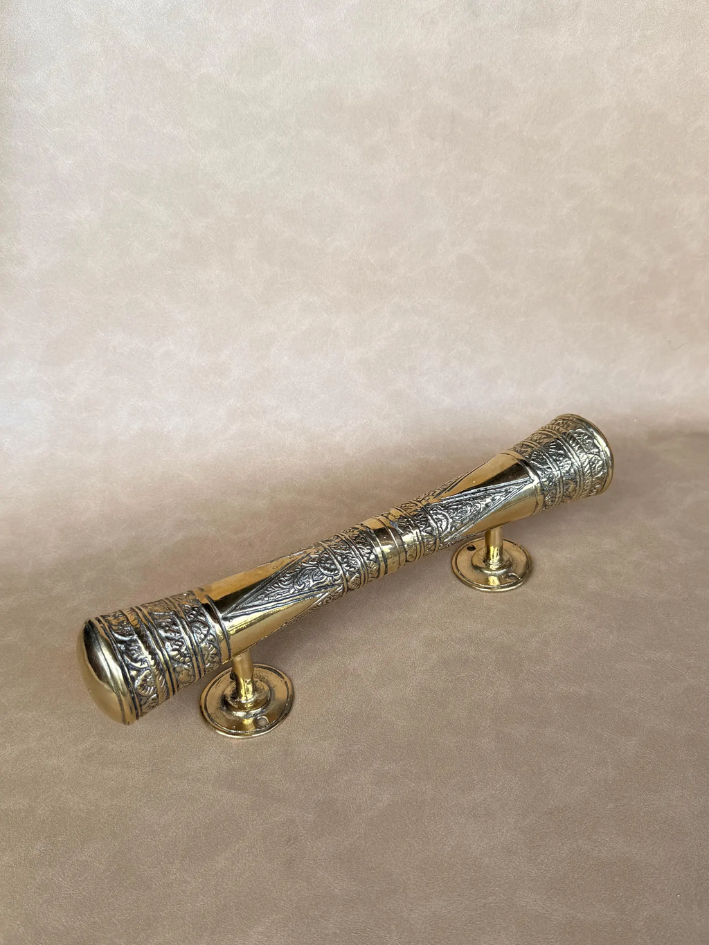 Single brass oriental pull handle lying diagonally, showing its posts