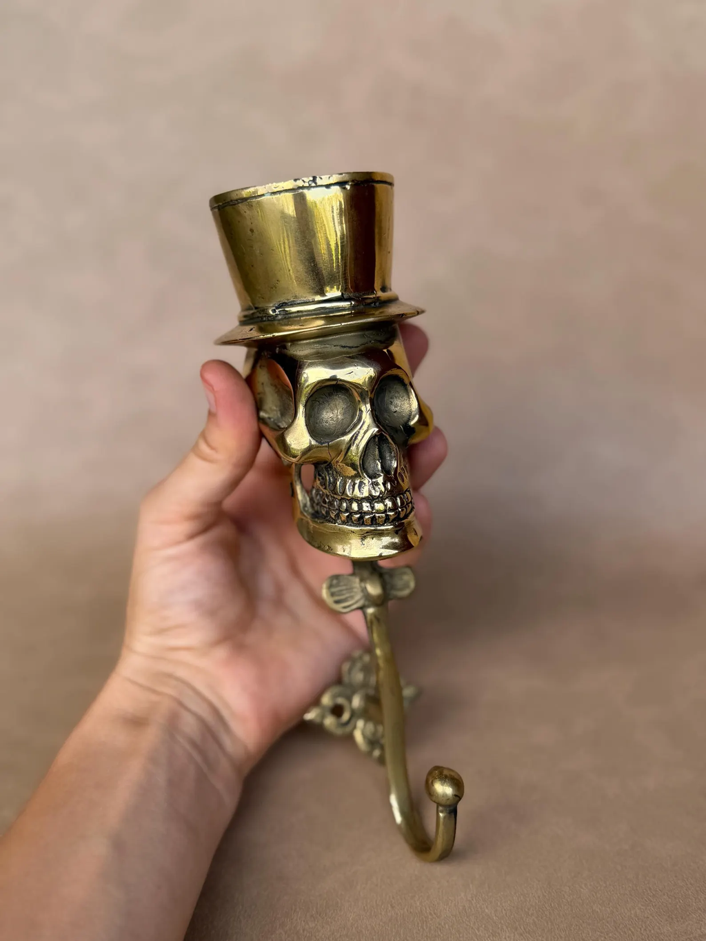 Hand holding the brass skull hook with top hat, front view with the curved hook below