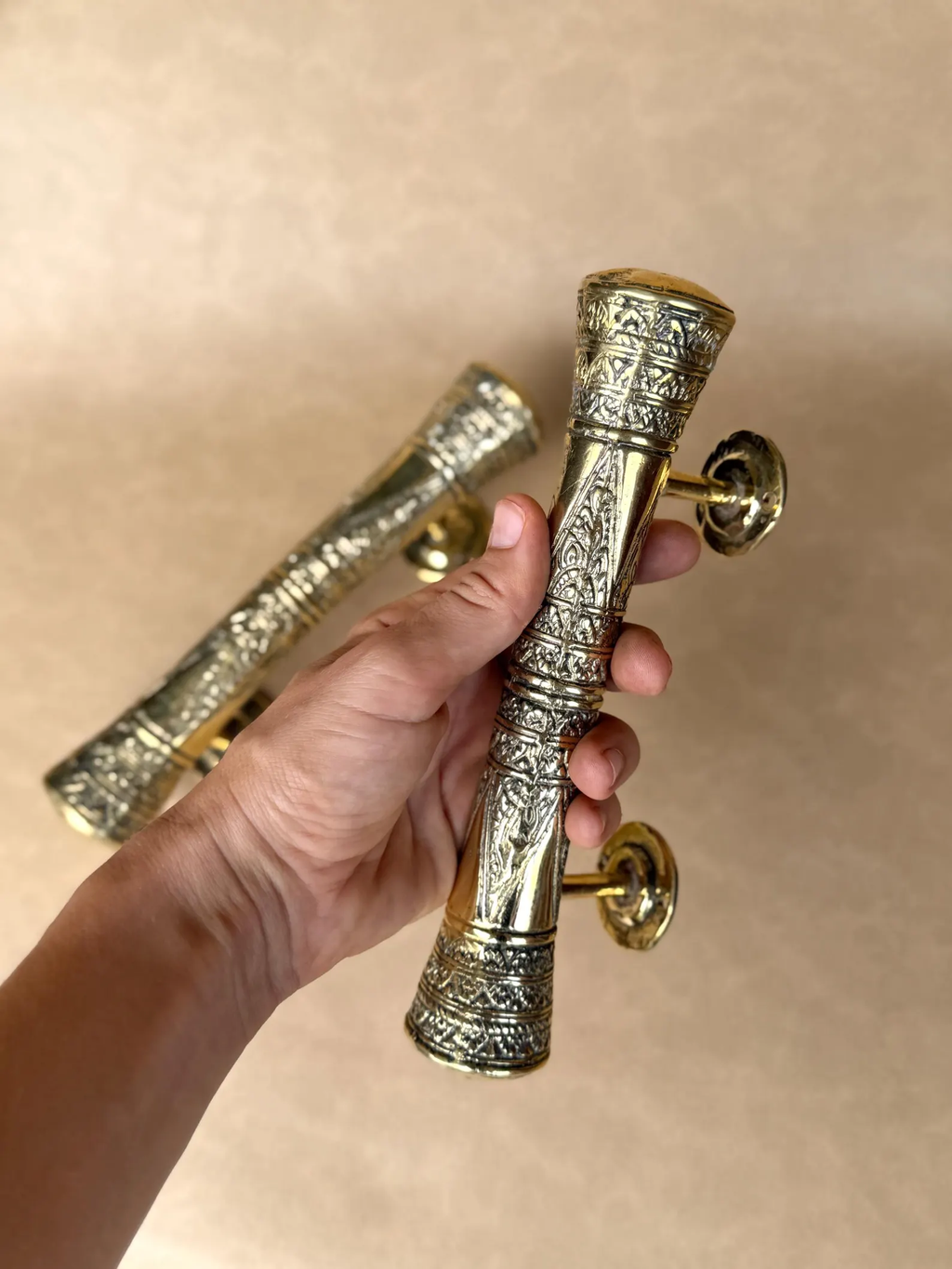 Hand holding an engraved brass handle with a second handle behind it