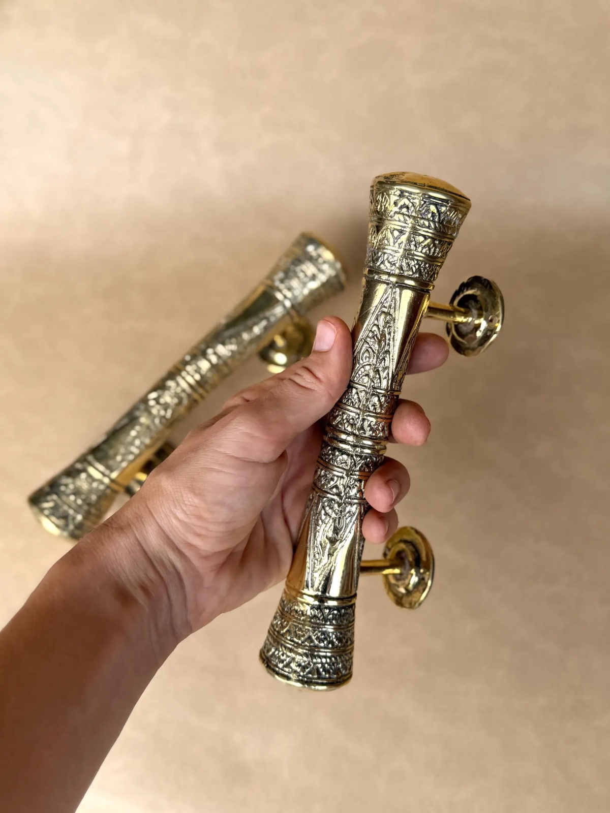 Hand holding an engraved brass handle with a second handle behind it