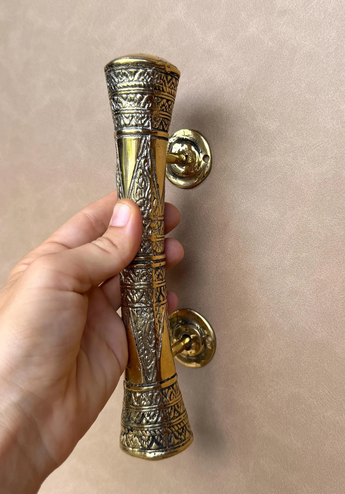 Hand holding a brass oriental cabinet pull, showing the mounting posts