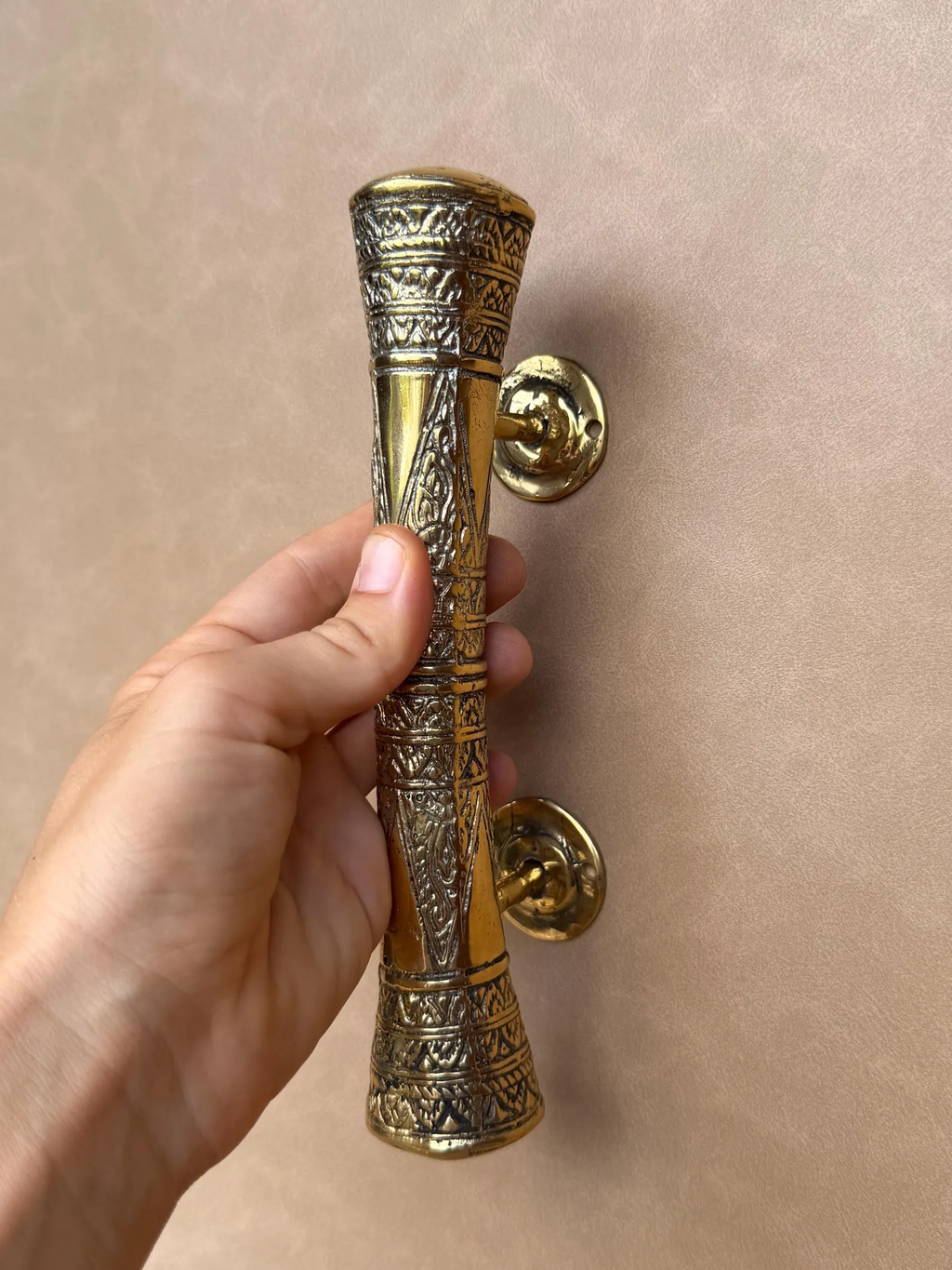 Hand holding the engraved brass door handle, front view