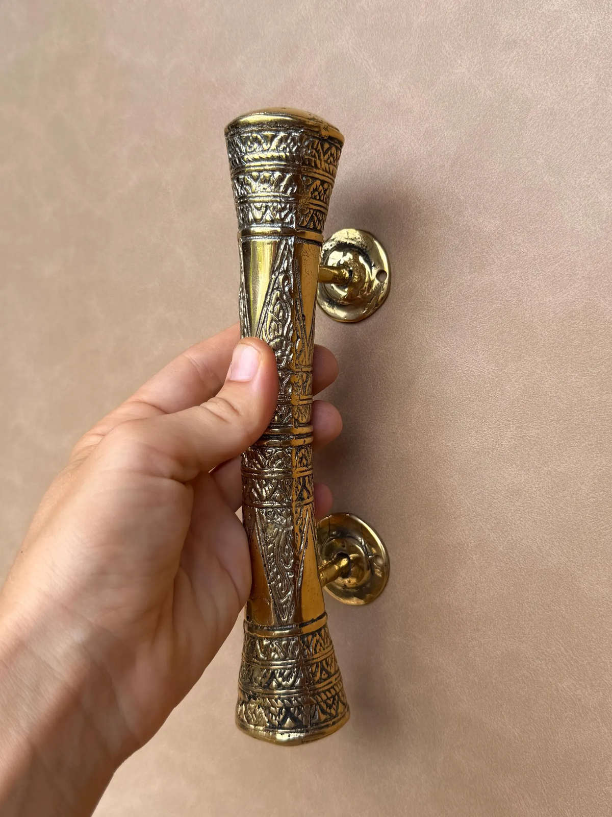 Hand holding the engraved brass door handle, front view