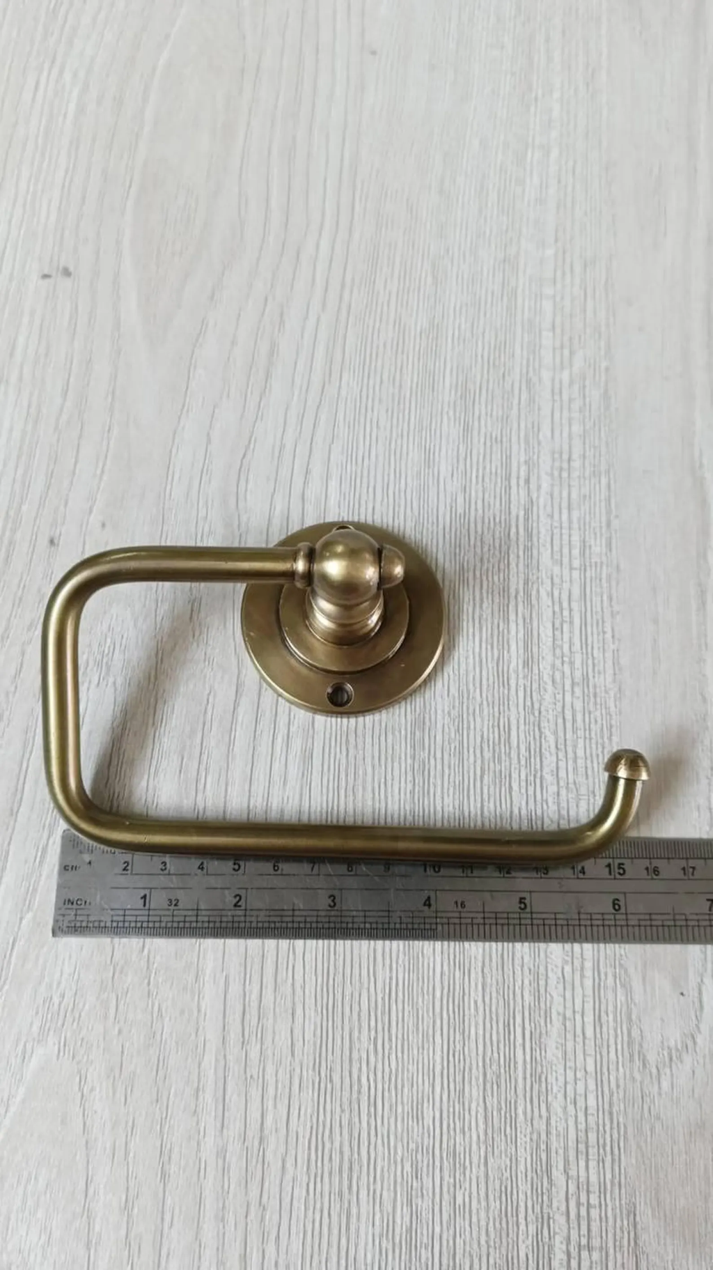 Brass toilet paper holder next to a ruler showing its 15 cm length