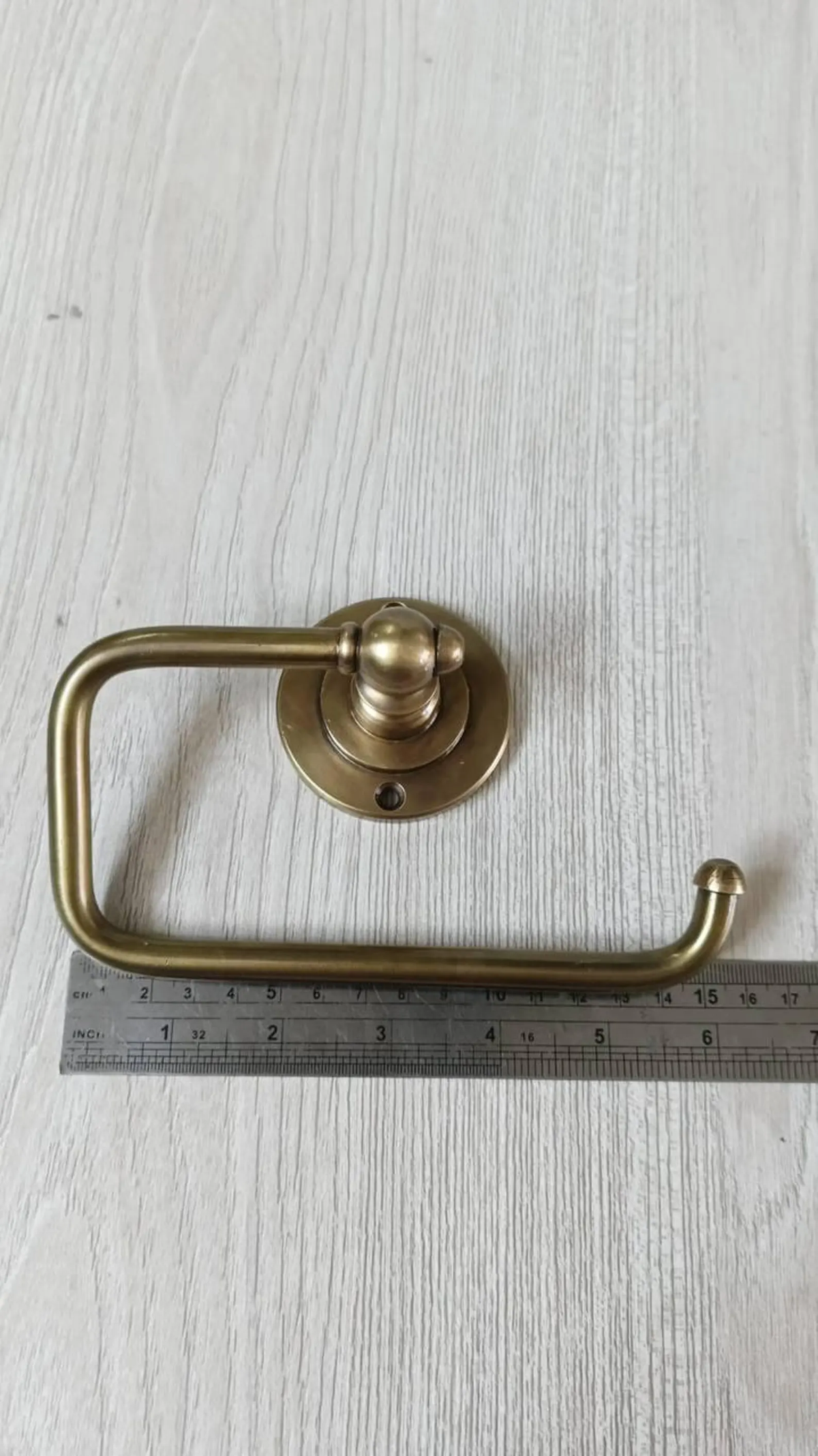 Brass toilet paper holder next to a ruler showing its 15 cm length