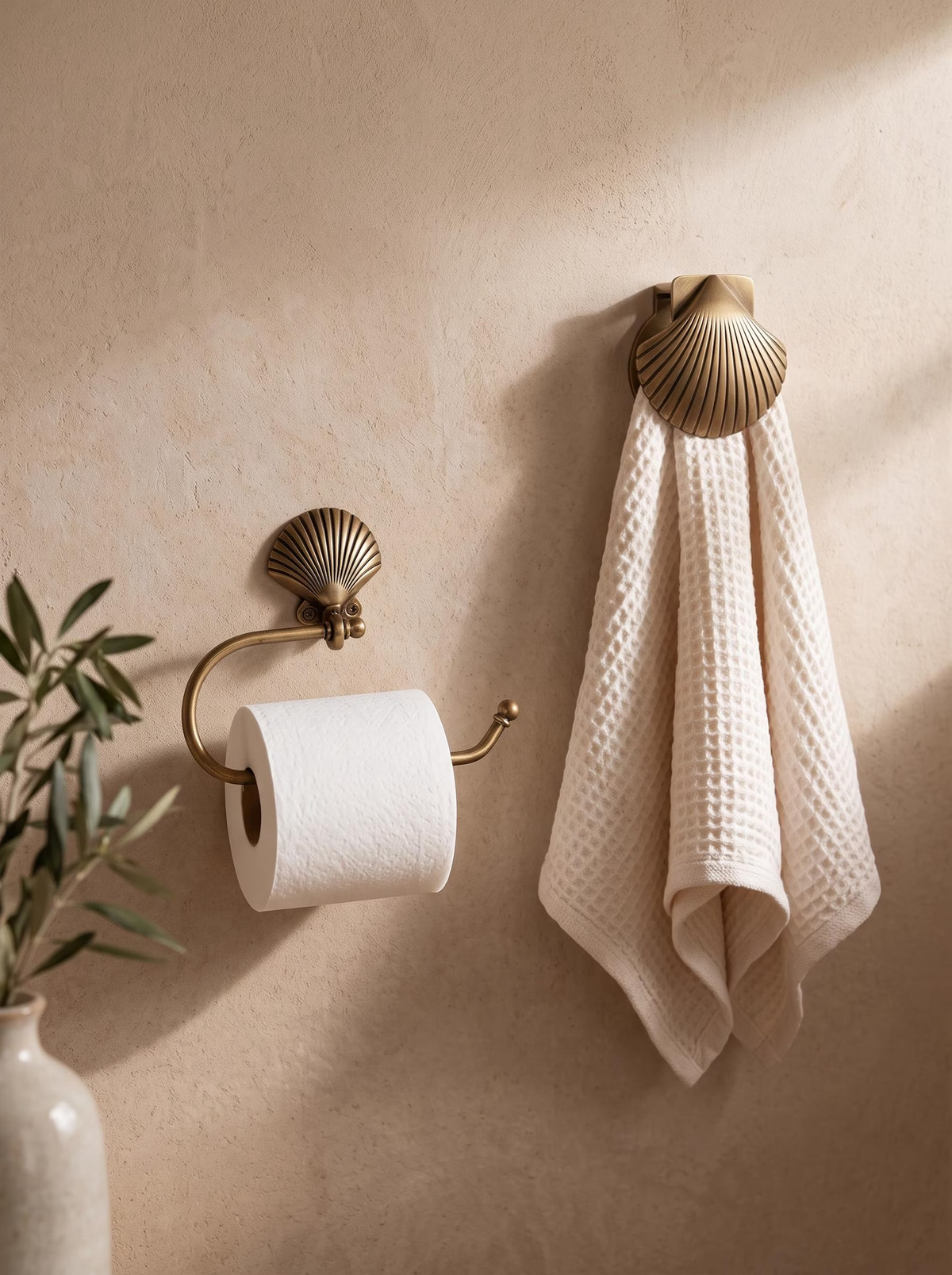 Brass shell toilet paper holder and matching shell clip holding a waffle towel on a beige plaster wall