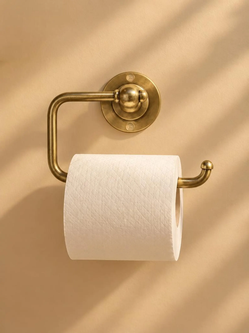 Antique brass toilet paper holder with a white roll, mounted on a warm beige wall