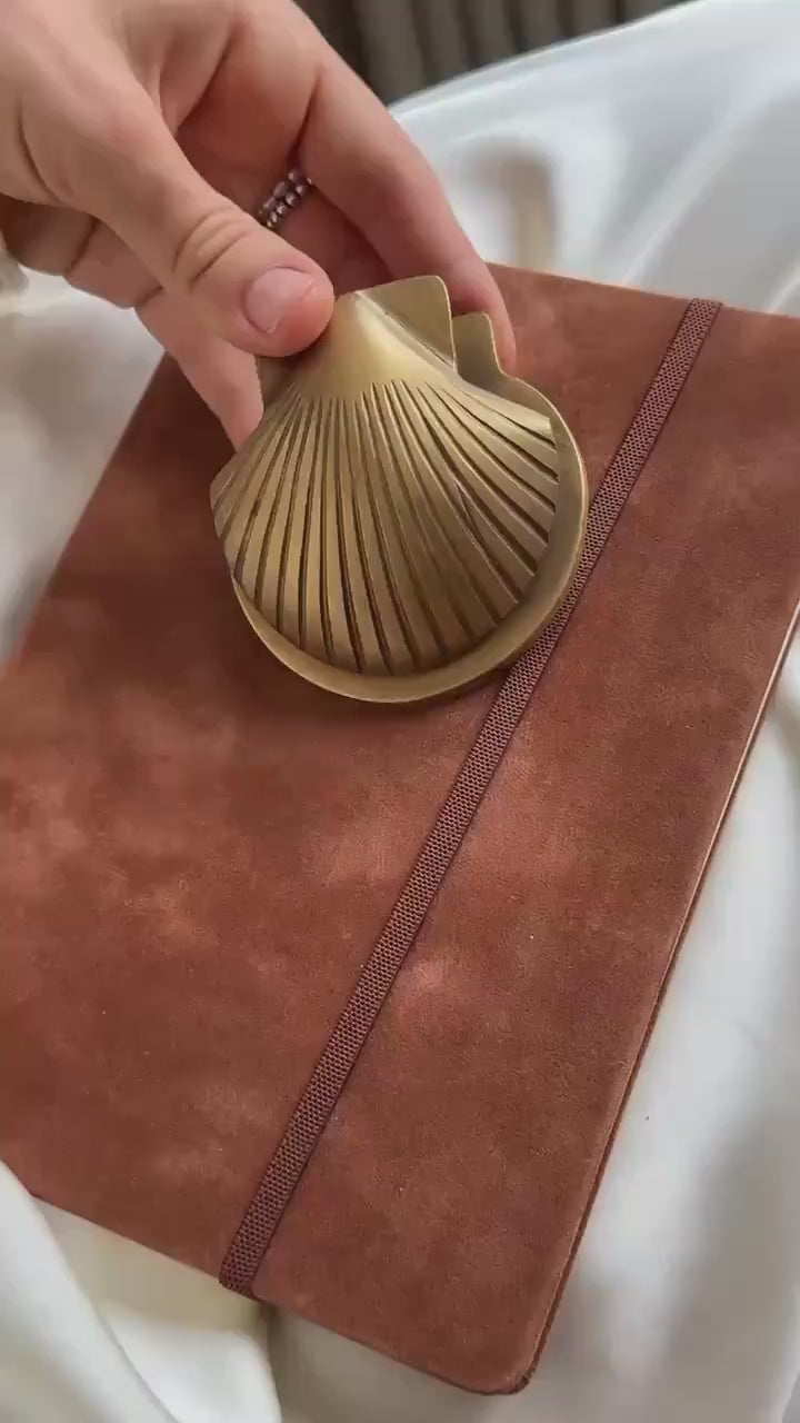 Video of a hand showing the brass shell clip on a suede notebook