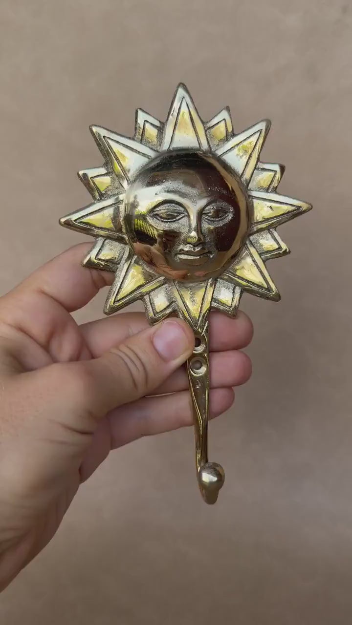Video of a hand holding the brass sun face wall hook against a taupe background